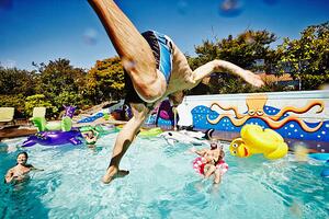 Umělecká fotografie Man in mid air jumping into pool during party, Thomas Barwick, (40 x 26.7 cm)