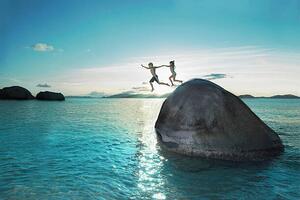 Fotografie Two kids holding hands jumping off rock into sea, Gary John Norman, (40 x 26.7 cm)